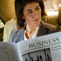 female executive reading newspaper back of limousine